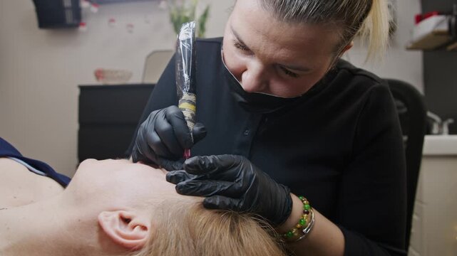 Watch as a skilled beautician expertly tattoos perfect eyebrows using a specialized machine. Close-up on the intricate application and careful finishing touches for stunning brows