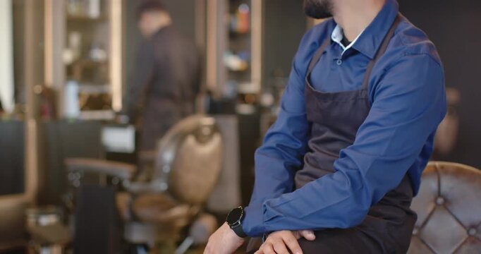 Camera pulling back showing male barber aproned turning to moving staff smiling in shop, copy space