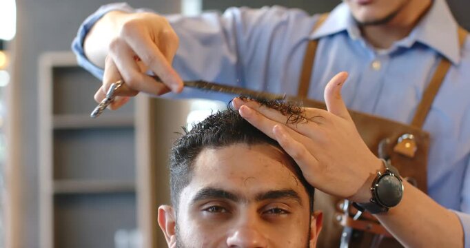 African American man sitting in barber chair, barber combing and trimming top hair with scissors