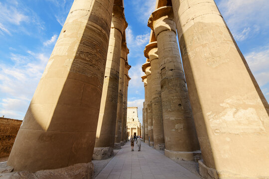 Tourists and Egyptian guides walk through the Grand Colonnade Hall of papyrus bud columns at the Great Court of Ramses II, at Luxor Temple, Luxor Egypt.