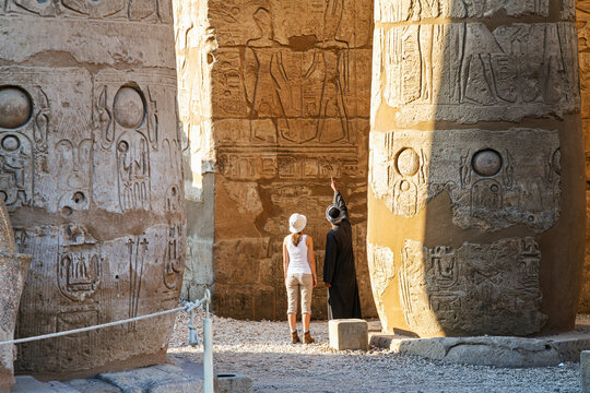 A private Egyptian guide and a female tourist admire the monumental sandstone columns at the Great Hypostyle Hall inside the Karnak Temple Complex in Luxor Egypt.