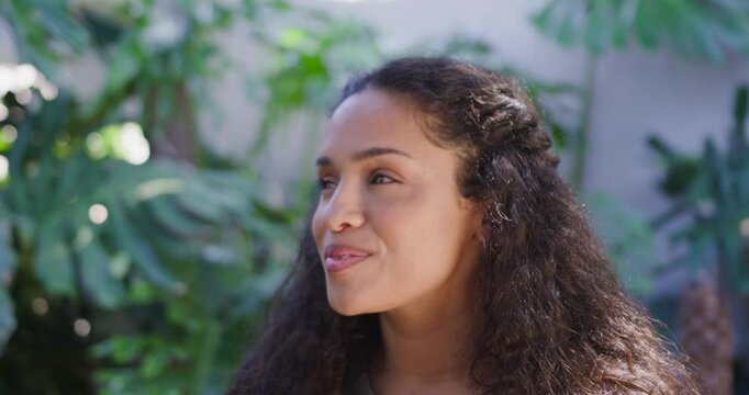 African American woman 20s reacting to offscreen cue, turning, smiling in garden with large leaves