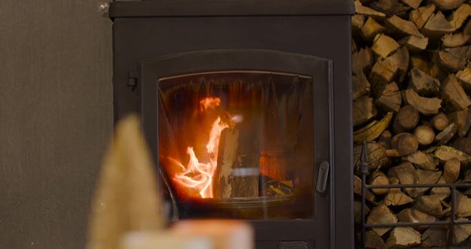 Hot embers are igniting upright log inside wood stove, flames climbing, charring log, warming home