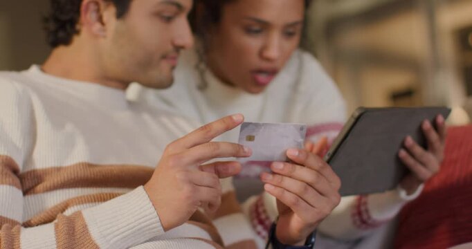 Couple leaning, man holding EMV chip card aligning with tablet on couch while verifying payment