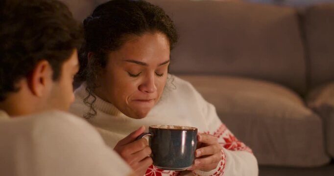 African American couple on couch woman in white sweater sipping then testing hot large mug, smiling