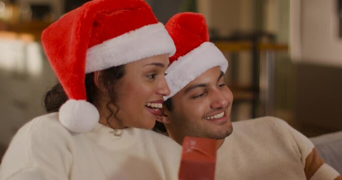 African American couple sitting on couch, reacting to off-screen surprise, smiling with Santa hats