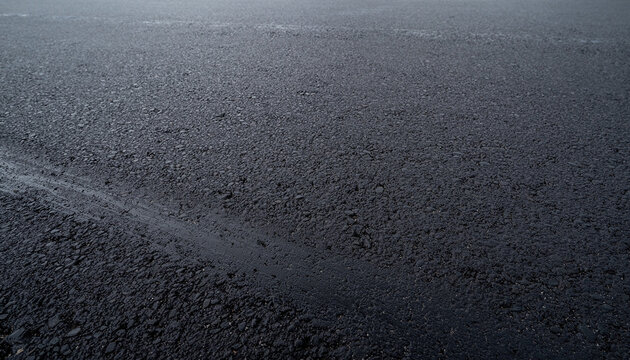Close-up view of a dark, textured asphalt road surface with subtle wet streaks and granular details.