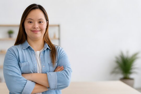 Portrait of a confident young woman with Down syndrome smiling with arms crossed in a bright modern office, professional lifestyle photography representing diversity, inclusion, and empowerment