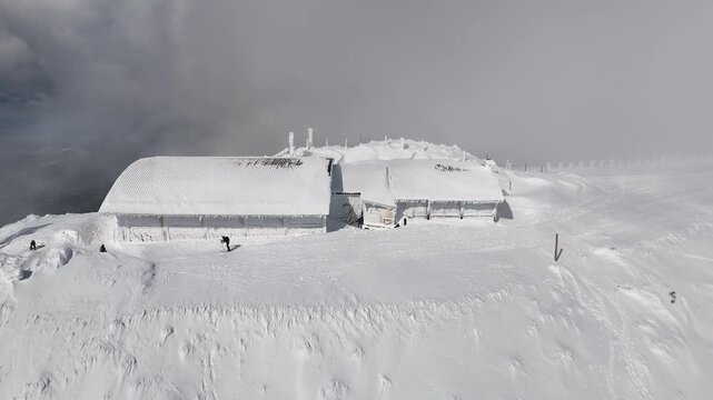 Aerial drone footage of the snow covered mountain refuge near Bola del Mundo at Puerto de Navacerrada, Sierra de Guadarrama, Madrid, Spain, with rime ice and a skier