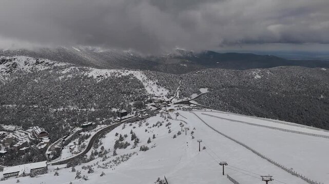 Aerial drone footage of the ski resort at Puerto de Navacerrada, Sierra de Guadarrama, Madrid, Spain, with snow covered slopes, chairlifts, and mountain ranges