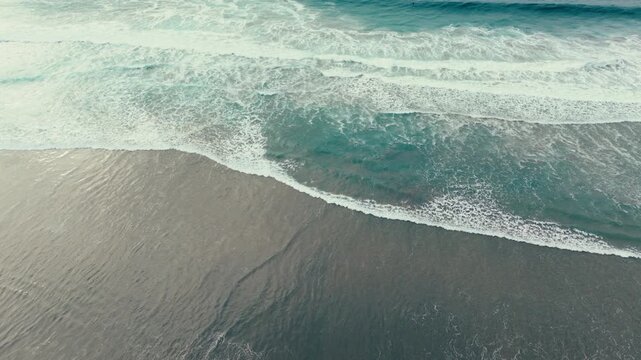 Aerial drone view of ocean waves rolling onto Pacific Beach shoreline in San Diego California under cloudy skies