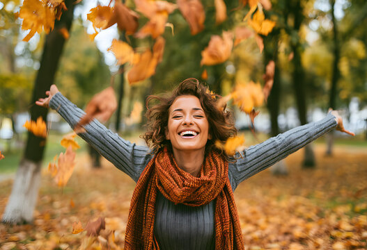 A joyful woman chuckling as she tosses leaves in the autumn at the city park.