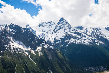 Obraz premium Majestic snow-capped mountains tower under a blue sky with clouds, revealing rugged terrain and green valleys in the foreground
