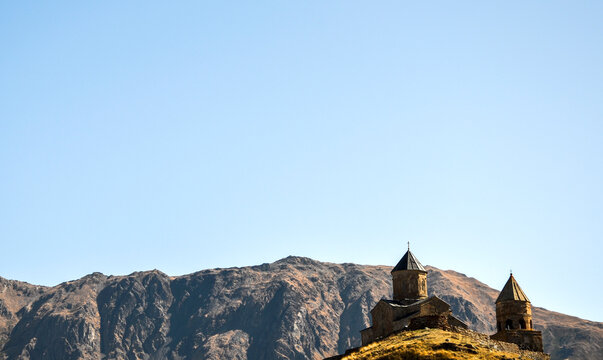 Ancient stone historic Gergeti Trinity Church sitting atop its high mountain hill against the massive, rugged backdrop of the Caucasus Range near Kazbegi, Georgia