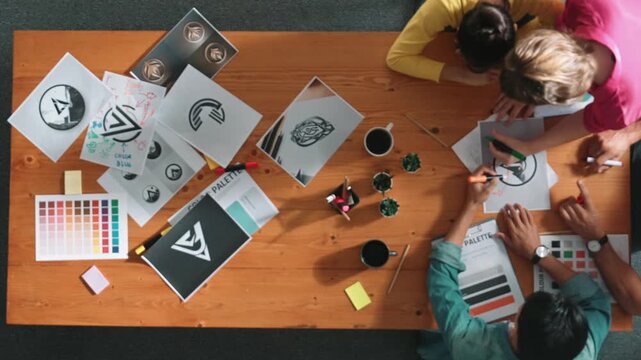 Top view of designer writing and designing logo graphic at meeting. Closeup of business man working on colored palettes and writing idea on sticky notes on table with equipment and paper. Symposium.