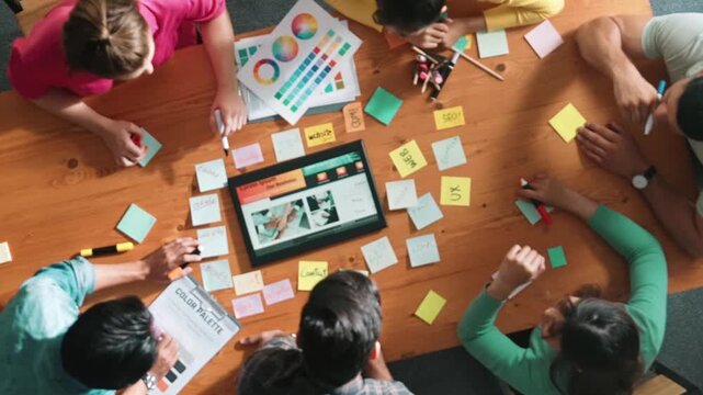 Top view of business people working together to design web design. Aerial view of designer brainstorming and discussing about website interface and looking at tablet with digital design. Symposium.