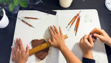 Rolling out brown modeling clay with a wooden rolling pin © Дарʼя Сидорова
