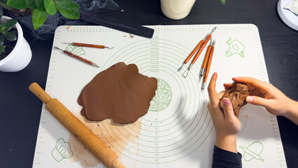 Rolling out brown modeling clay with a wooden rolling pin © Дарʼя Сидорова