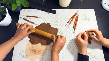 Rolling out brown modeling clay with a wooden rolling pin © Дарʼя Сидорова