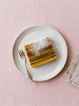 Sliced Rainbow Layer Cake with Coconut Dusting on Pastel Plate