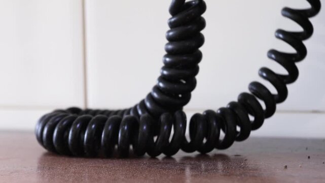 Black spiral telephone cord on a wooden surface against a white tiled wall background