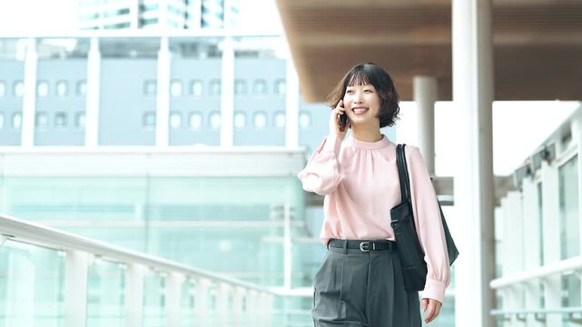 オフィス街を歩きながらスマートフォンで話す女性・ビジネスウーマン, Businesswoman Walking Through an Office District While Talking on a Smartphone