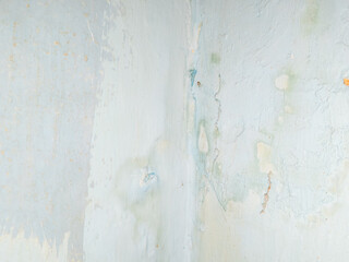 Abstract background of a weathered and distressed wall with peeling paint and plaster in faded light blue and beige tones, showcasing aged texture and grunge details. © Haerudin