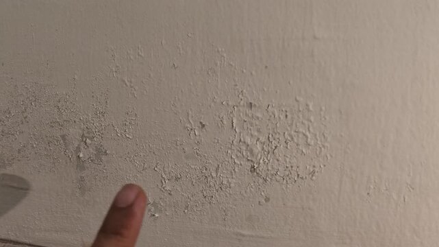 Close up shot of a hand pointing at bubbling and blistering paint on a wall caused by indoor water dampness and moisture damage.
