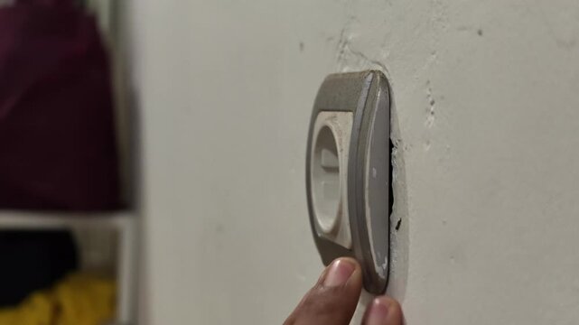 Person hand installing a dual socket extension plug adapter onto a wall outlet, plugging a cable, and toggling the neon switch buttons.
