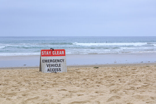 Emergency vehicle access sign on the sandy Pacific Beach with ocean waves and surfers in the background, San Diego, California