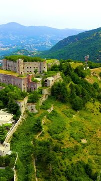 Vertical video. Genoa, Italy. Forte Sperone, a massive stone fortress with grass-covered ramparts, Drone footage over the Ligurian hills and distant coastline. Drone footage, Point of interest. Rich 
