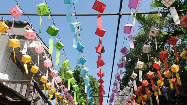 Rows of vivid traditional Lanna paper lanterns in many colors hanging and swaying at a Buddhist temple in northern Thailand. Vacation and travel concept