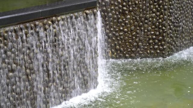 Gentle waterfall cascades over a textured stone wall into a tranquil pool