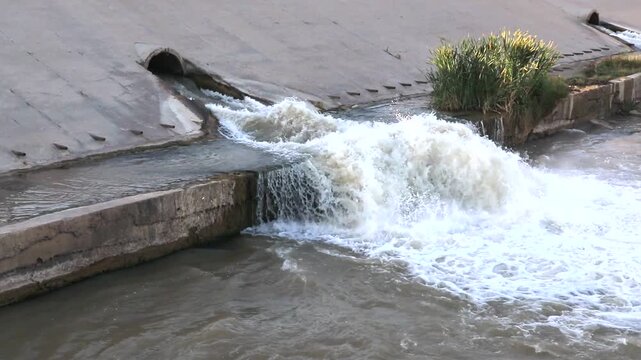 Video clip featuring the loud sound of water gushing from a storm drain into a concrete channel. Use for environmental projects, relaxation, foley, or stock footage of urban water flow.