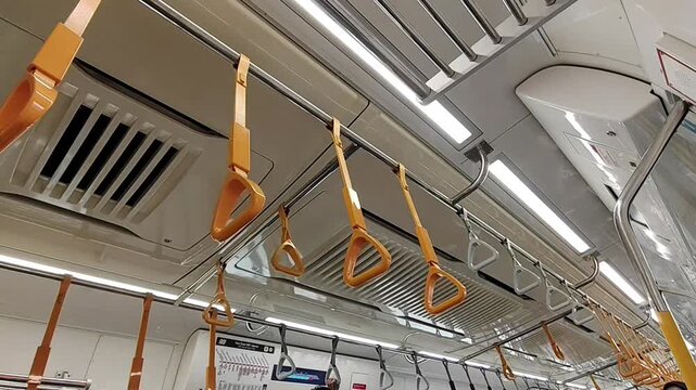 Interior view of a modern train carriage showing a row of yellow triangular hand grips hanging from a metal handrail on the ceiling, designed for standing commuters.