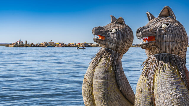 The traditional balsa de totora has decorations in the shape of puma heads woven from reeds on the bow of the boat. On the far shore, you can see the Uros floating island, village buildings. Blue lake