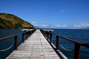 Fototapeta premium A wooden plank road leading to the sea on Gili Mori beach, Labuan Bajo, East Nusa Tenggara, Indonesia, with a blue sky and beautiful beach as a backdrop