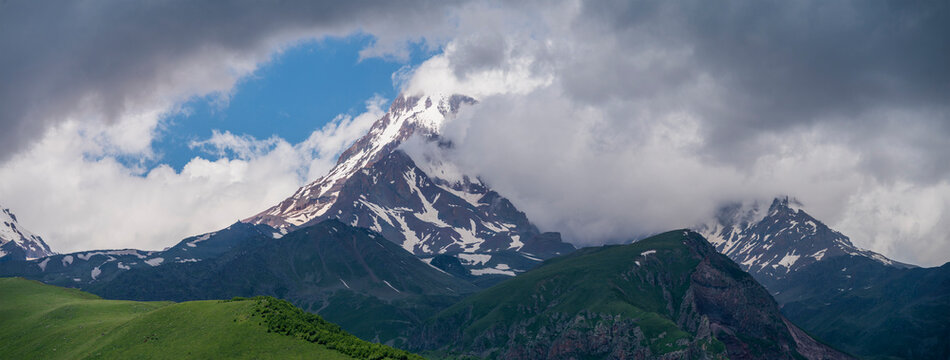 Panoramic Caucasus mountains landscape with Mount Kazbek peak and green hills