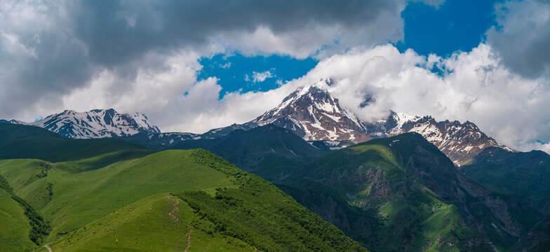 Epic Caucasus mountain landscape with sunlit green valley and Mount Kazbek peak