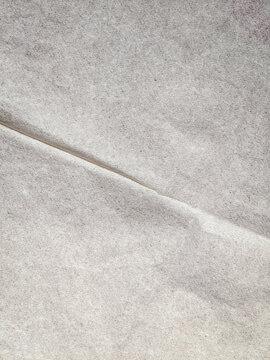 Textured white tissue paper background with diagonal crease. Macro shot of translucent white tissue paper featuring a natural fibrous texture, a prominent diagonal fold line, and soft lighting.