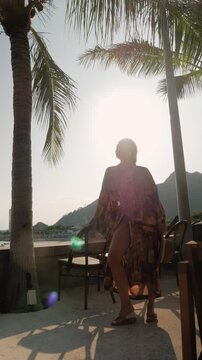 tylish woman in bikini and patterned beach kimono at tropical waterfront resort during golden hour