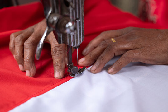 Indonesian Independence Day. A senior woman's hands are sewing the red and white flag using a sewing machine.