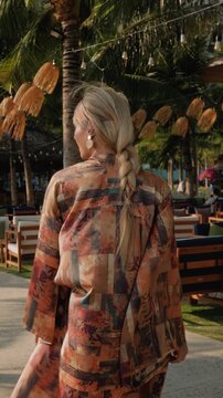 Stylish woman wearing patterned beach kimono walking through tropical resort 