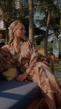 Relaxed woman in patterned beach kimono enjoying sunshine at tropical resort lounge  