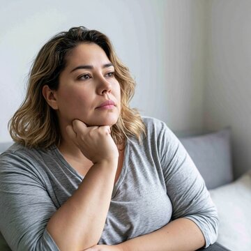 Pensive sad overweight obese woman sitting at her bedroom looking away very worried	
