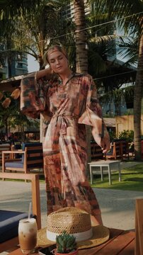 Stylish woman wearing patterned beach kimono walking through tropical resort 