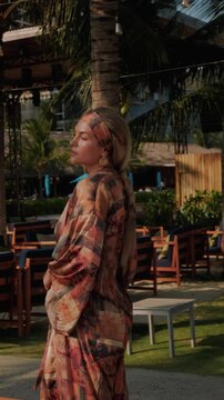 Stylish woman wearing patterned beach kimono walking through tropical resort 