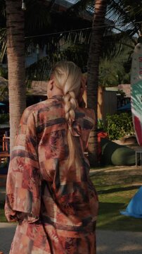 Stylish woman wearing patterned beach kimono walking through tropical resort 