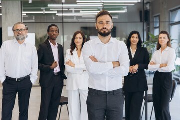 Fototapeta premium Diverse business team standing in office, male leader with arms crossed, coworkers expressing corporate unity and success