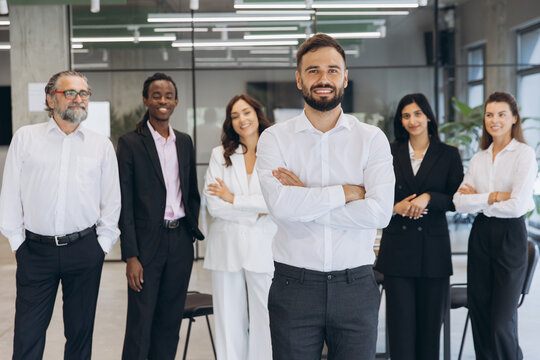 Diverse business team standing in office with male leader crossing arms, symbolizing successful corporate teamwork and professionalism